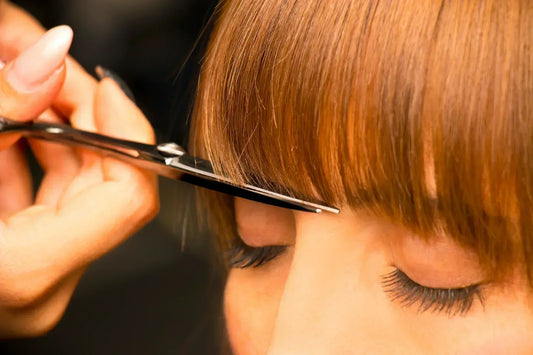 a close up image of a scissor trimming a woman bang