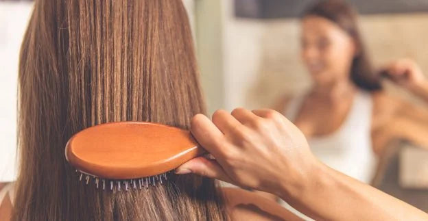 woman brushing her hair while looking at the mirror